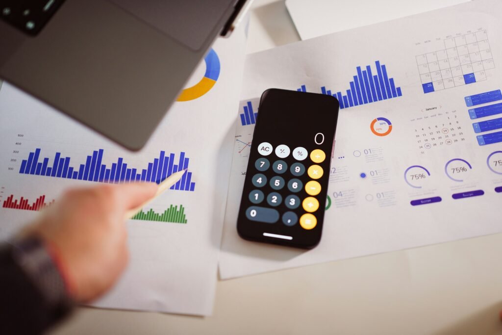 Calculator, laptop, notebook, and smartphone arranged on a wooden desk, representing AI productivity, business planning, and digital work.