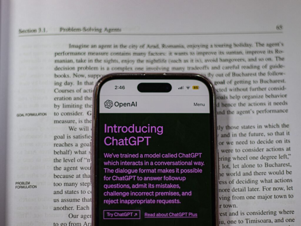 Close-up of an iPhone displaying the ChatGPT webpage on top of an open book, representing AI technology, digital learning, and online productivity.