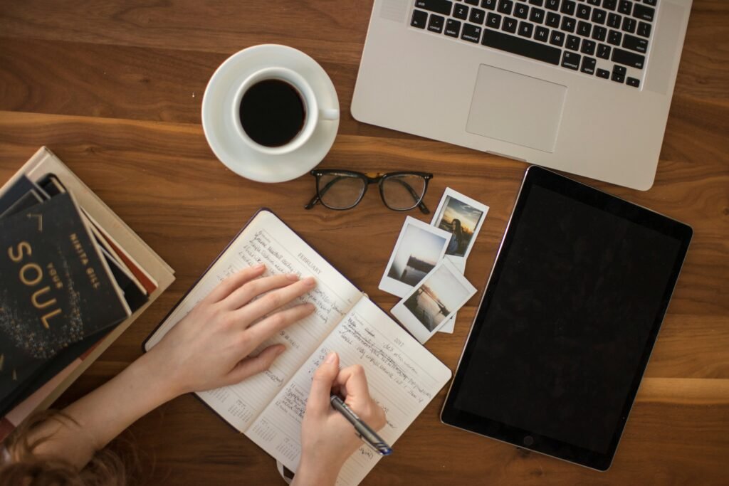 Person writing notes in a notebook beside a laptop, illustrating effective ChatGPT study habits like taking notes, reviewing answers, and applying AI learning tips.