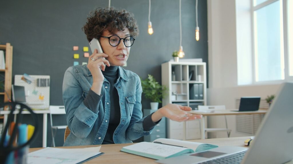 **Alt Text:**
Student using a laptop while talking on the phone, representing someone asking ChatGPT difficult questions to better understand complex topics and solve challenging study problems.
