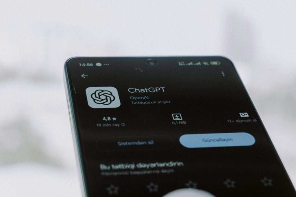 Smartphone displaying the ChatGPT app beside a laptop on a desk, illustrating mobile AI assistant use for productivity and everyday tasks.